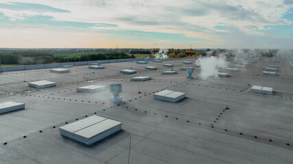 Fototapeta na wymiar Large roof of factory with roof ventilators, steam coming out from them, drone shot from above
