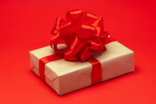 Close up shot of gift box wrapped in craft paper and decorated with satin ribbon bow, isolated on red background