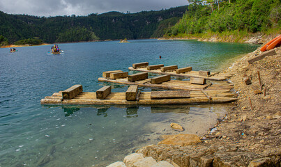 Lakeside Serenity: Wooden Pier on a Chiapas Lake, Azure Waters, Lush Trees, Earthy Ground, Distant Boats, Overcast Day. Montebello's Lake.