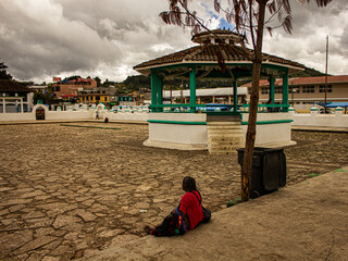 Cultural Encounter: Indigenous Woman by Turquoise Kiosk in San Juan Chamula Churchyard, Chiapas, Mexico. Cloudy, Cool Day Vibes.