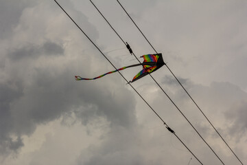 Colorful kite caught on power cables in a cloudy sky