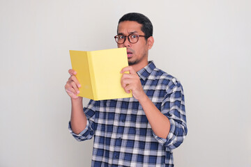 Adult Asian man showing shocked expression while holding a book