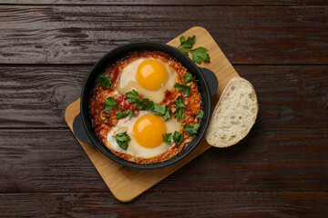 Delicious shakshuka in frying pan on wooden table, top view