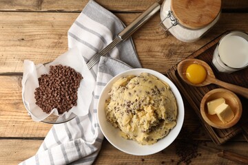 Chocolate chip cookie dough in bowl and ingredients on wooden table, flat lay
