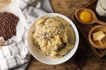 Chocolate chip cookie dough in bowl and ingredients on wooden table, flat lay