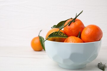 Bowl with fresh ripe tangerines and leaves on white table, space for text