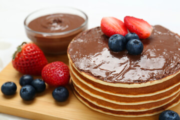 Tasty pancakes with chocolate paste and berries on table, closeup