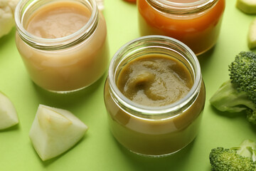 Obraz na płótnie Canvas Jars with healthy baby food, broccoli and apple on light green background, closeup
