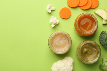 Jars with healthy baby food and fresh vegetables on light green background, flat lay. Space for text