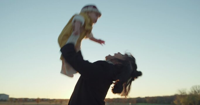 Mom doing airplane with happy baby and holding him in the air in a field at sunset