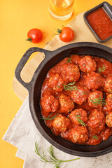Frying pan of tasty meat balls with tomato sauce and dill on yellow background