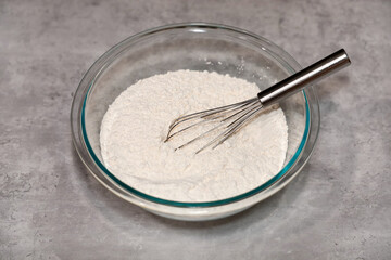 Whole wheat white flour in a glass mixing bowl and a whisk inside.