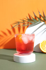 Glass of delicious Negroni cocktail with ice cubes and palm leaf on color background
