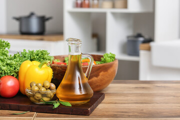 Jug with oil, lettuce, olives and vegetables on table in kitchen