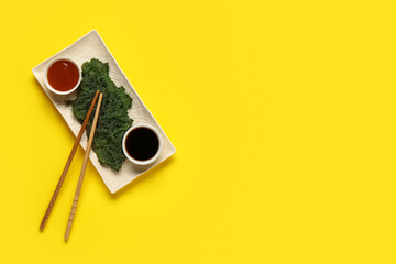 Plate with healthy seaweed, sauces and chopsticks on yellow background