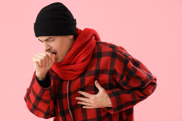 Ill young man in winter clothes coughing on pink background