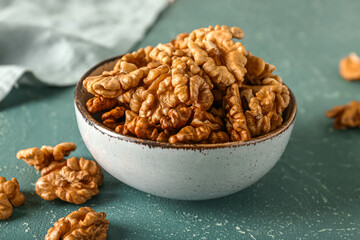 Bowl of tasty walnuts on green background