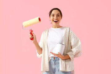 Young woman with paint roller and can on pink background