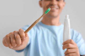 Handsome young man with tooth brush and paste on grey background. Dental care concept