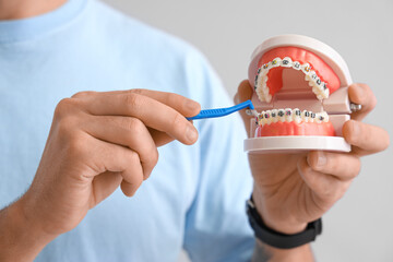 Handsome young man holding model of jaw with dental braces and toothbrush on grey background....