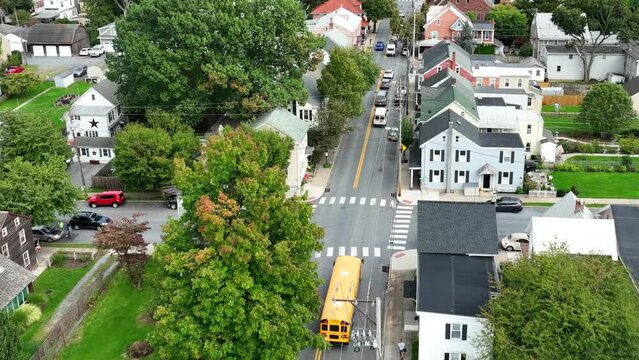 Yellow school bus driving on road. Aerial tracking shot zoom out revealing small town USA.