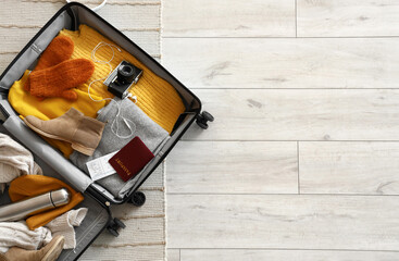 Open suitcase with winter clothes and accessories on carpet, top view