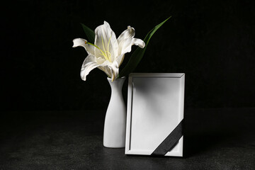 Blank funeral frame and vase with lily flower on dark background