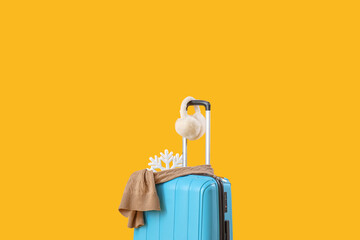 Suitcase with snowflake, earmuffs and scarf on yellow background