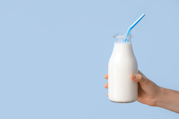 Hand holding bottle of milk with straw on light blue background
