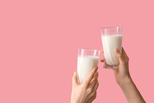 Hands clinking glasses of milk on pink background
