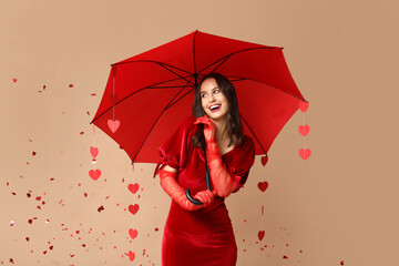 Beautiful young woman holding umbrella with paper hearts and confetti on brown background. Valentine's Day celebration