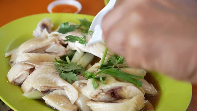 close up view while use spoon and fork to grab homemade singapore hainan chicken in big plate at hawker center,famous dish of singapore delicious Steamed Chicken to eat with rice