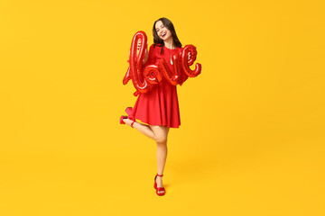Happy young woman with air balloons in shape of word LOVE on yellow background. Valentine's Day celebration