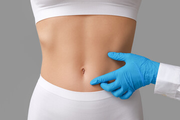 Young woman with flat belly and plastic surgeon on light background, closeup - obrazy, fototapety, plakaty