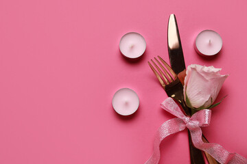 Cutlery with bow, rose and candles on pink background. Valentine's Day celebration
