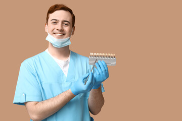 Male dentist with dental shade guide on beige background. World Dentist Day
