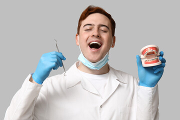 Male dentist with dental explorer and jaw model on grey background. World Dentist Day