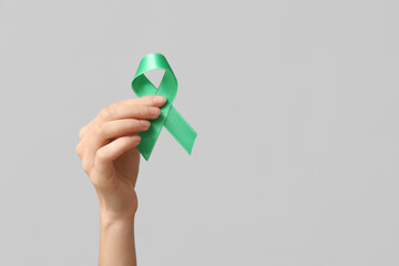 Female hand with green ribbon on grey background. Glaucoma awareness concept