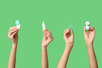 Female hands with containers for contact lenses, tweezers and eye drops on green background....
