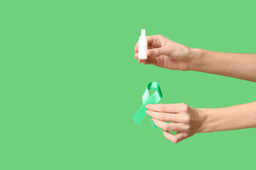 Female hands with ribbon and eye drops on green background. Glaucoma awareness concept