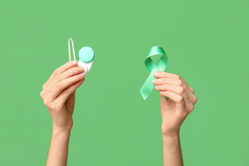 Female hands with ribbon, tweezers and container for contact lenses on green background. Glaucoma...