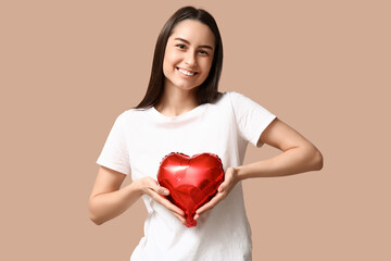 Beautiful young woman with heart-shaped air balloon on beige background