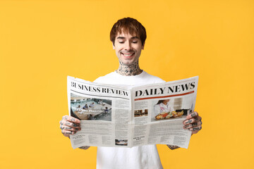 Handsome young man with newspaper on yellow background