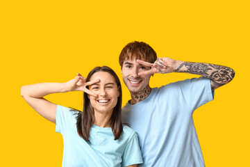 Young couple showing victory gesture on yellow background