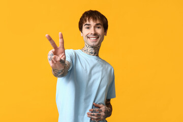 Handsome young man showing victory gesture on yellow background
