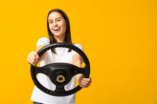 Beautiful young woman with steering wheel on yellow background