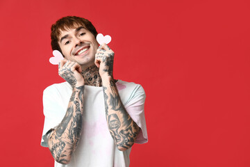 Handsome young man with paper hearts on red background