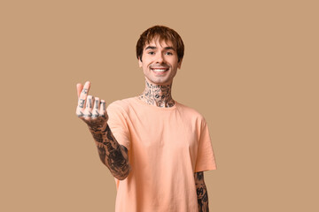 Handsome young man making heart with fingers on beige background
