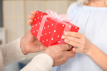 Mature couple greeting his wife with gift at home, closeup