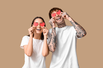 Funny young couple with paper hearts on beige background